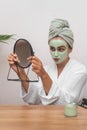 woman pampering day, applying green clay mask and smiling at her radiant reflection in the mirror.