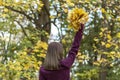 Woman in park holds autumn leaf bouquet. View from back