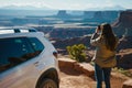 woman parked at a scenic overlook, taking a photo with a phone