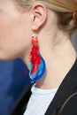 Woman with parrot earring with red and blue feathers before Gabriele Colangelo fashion show, Milan Fashion