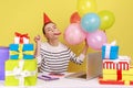 Woman with party cone sitting workplace among gifts and balloons, blowing horn, celebrating birthday Royalty Free Stock Photo