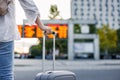 Woman passenger with suitcase is checking arrival and departure board schedule timetable at train or bus station Royalty Free Stock Photo