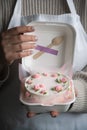 Woman pastry shef wearing white apron and holding small bento cake decorated with cream cheese pink flowers. Woman hands hold Royalty Free Stock Photo