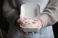 Woman pastry shef wearing white apron and holding small bento cake decorated with cream cheese pink flowers. Woman hands hold Royalty Free Stock Photo