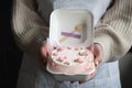 Woman pastry shef wearing white apron and holding small bento cake decorated with cream cheese pink flowers. Woman hands hold Royalty Free Stock Photo