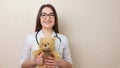 Woman pediatrician with glasses holds teddy bear on beige