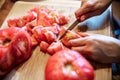 Woman is peeling a lot of red fresh and boiled tomatos with a knife, preparing for cooking a sauce