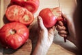 Woman is peeling a lot of red fresh and boiled tomatos with a knife, preparing for cooking a sauce