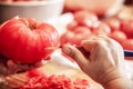 Woman is peeling a lot of red fresh and boiled tomatos with a knife, preparing for cooking a sauce