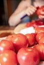 Woman is peeling a lot of red fresh and boiled tomatos with a knife, preparing for cooking a sauce