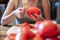 Woman is peeling a lot of red fresh and boiled tomatos with a knife, preparing for cooking a sauce