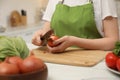 Woman peeling onion at table in kitchen, closeup. Preparing vegetable