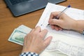 woman with a pen in her hands at a table with a wad of cash dollars calculates income for taxes