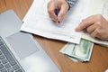 woman with a pen in her hands at a table with a wad of cash dollars calculates income for taxes