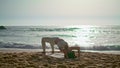 Woman performing bridge pose at sunrise. Girl practicing yoga asana on beach.