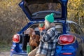 Woman pet owner enjoying tea sitting in car trunk with dog admiring nature in forest on weekend. Royalty Free Stock Photo