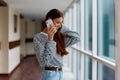 A woman with a phone in her hands talking and laughing while looking out the window at the city. High quality photo Royalty Free Stock Photo