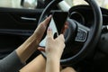 A woman with a phone sitting behind the wheel of a car.