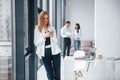 Woman with phone standing in front of group of young successful team that working and communicating together indoors in Royalty Free Stock Photo