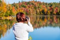 Woman photographer taking pictures of a lake surrounded by a forest at the peak of fall foliage colors Royalty Free Stock Photo