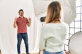 Woman photographer talking pictures of man posing as model at photography studio amazed and surprised looking up and pointing with Royalty Free Stock Photo