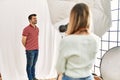 Woman photographer talking pictures of man posing as model at photography studio looking away to side with smile on face, natural Royalty Free Stock Photo