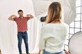 Woman photographer talking pictures of man posing as model at photography studio looking confident with smile on face, pointing Royalty Free Stock Photo