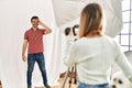 Woman photographer talking pictures of man posing as model at photography studio smiling happy doing ok sign with hand on eye Royalty Free Stock Photo