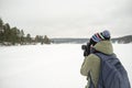 A woman photographer in warm clothes holds a camera in her hands and takes pictures of the winter landscape. Against the backdrop Royalty Free Stock Photo