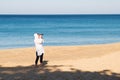 Woman photographer in a white thin tunic takes pictures on a sunny sandy beach