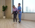 Woman physical therapist in blue uniform help an elderly to exercise and practice walking with Safety Transfer Belt. Atmosphere in