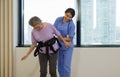 Woman physical therapist in blue uniform help an elderly to exercise and practice walking with Safety Transfer Belt. Atmosphere in