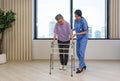 Woman physical therapist in blue uniform help an elderly to exercise and practice walking on walker or cane
