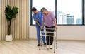 Woman physical therapist in blue uniform help an elderly to exercise and practice walking on walker or cane. Healthcare and