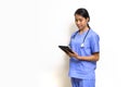 Woman physical therapist in blue uniform and stethoscope typing on tablet computer. Stand in front of white wall