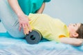 Woman at the physiotherapy doing physical exercises with her therapist, they using a massage roll. A chiropractor treats patient`