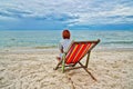 Woman picnicking and overlooking the sea sitting on a red chair at the beach Royalty Free Stock Photo