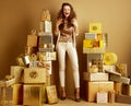 Woman among 2 piles of golden gifts in front of plain wall
