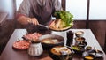 A woman pinching vegetables into hot pot by tongs with Wagyu A5 beef and sliced Kurobuta in Shabu clear soup with stream