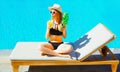 woman with pineapple drinks fruit juice from cup on deckchair over blue water pool background Royalty Free Stock Photo