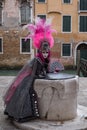 Woman in pink and black hand made costume with fan and ornate painted feathered mask at Venice Carnival