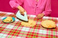 Woman in pink blouse ironing pancake on plaid tablecloth. Meme featuring unexpected ways to prepare food through humor.