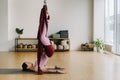 A woman in pink clothes does yoga on a suspended burgundy hammock in a bright gym