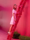 woman in a pink dress on a bright pink street sits on a staircase decorated with flowers