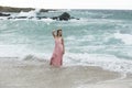 Woman in pink dress standing in crashing waves of ocean