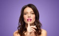 Woman with pink lipstick holding finger on mouth