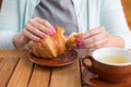 Woman with pink manicure is tearing a small piece from large croissant, front