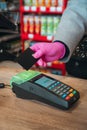 Woman in pink protective glove paying with contactless card at food store during quarantine. Closeup view of terminal Royalty Free Stock Photo