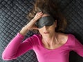 A woman with headache and blindfold on eyes lying on bed wtih pills in hand Royalty Free Stock Photo
