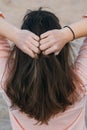 A woman in pink shirt holding her natural hair with both hands. Brunette woman with long hair, view from the back. Royalty Free Stock Photo